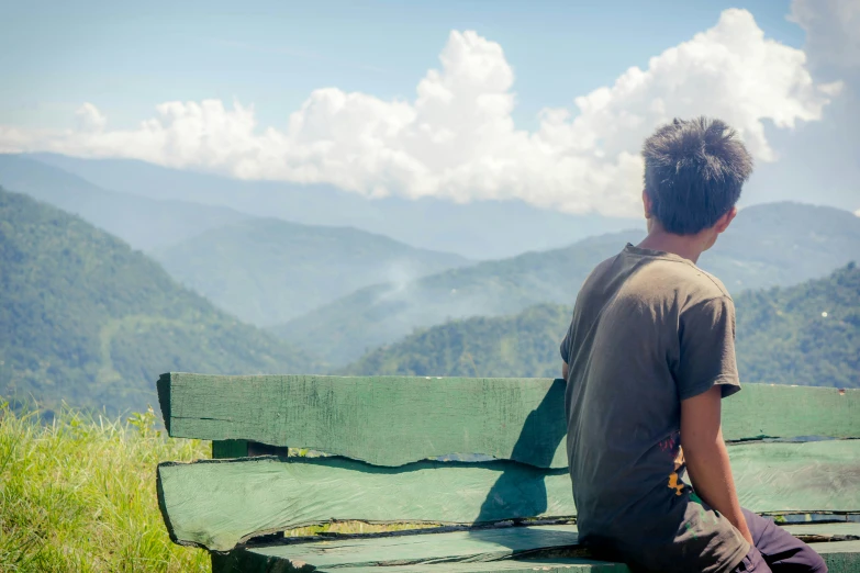 the boy sitting on the bench watches over the mountain range