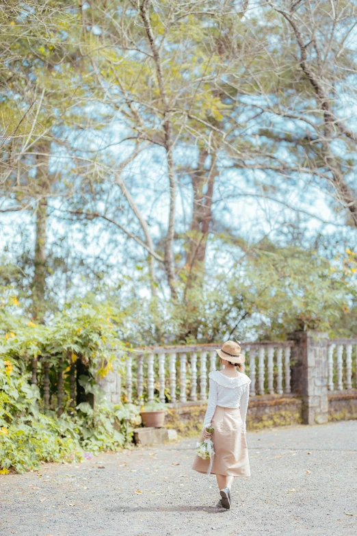 a lady wearing a tan dress is standing in front of the trees