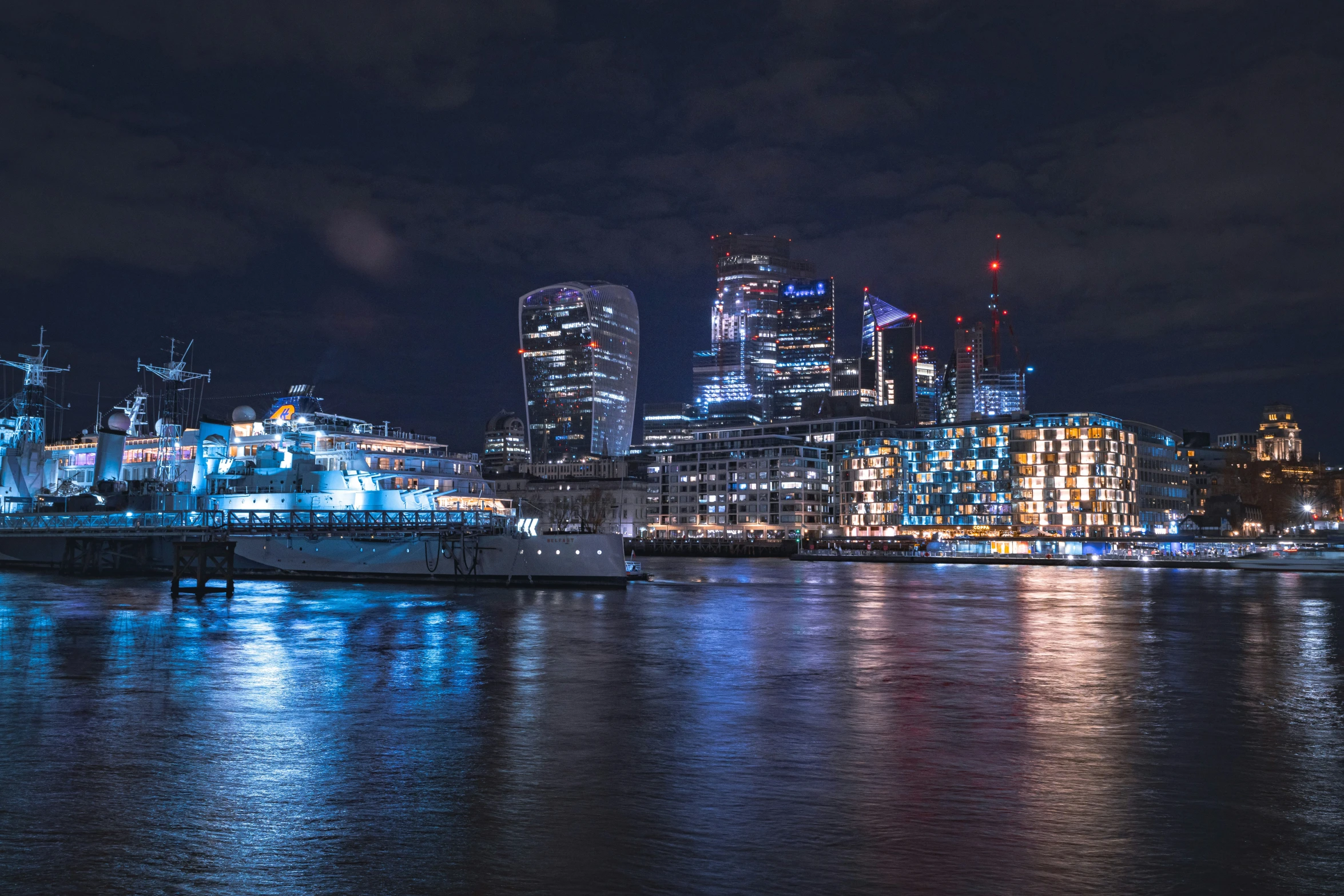 the view from a river at night, with lights on the buildings