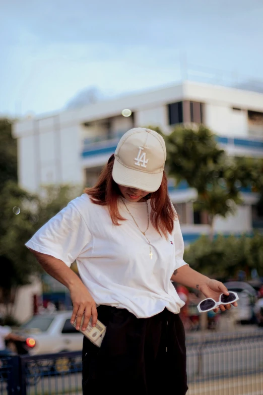 woman with baseball cap, sunglasses, and cap holding sunglasses
