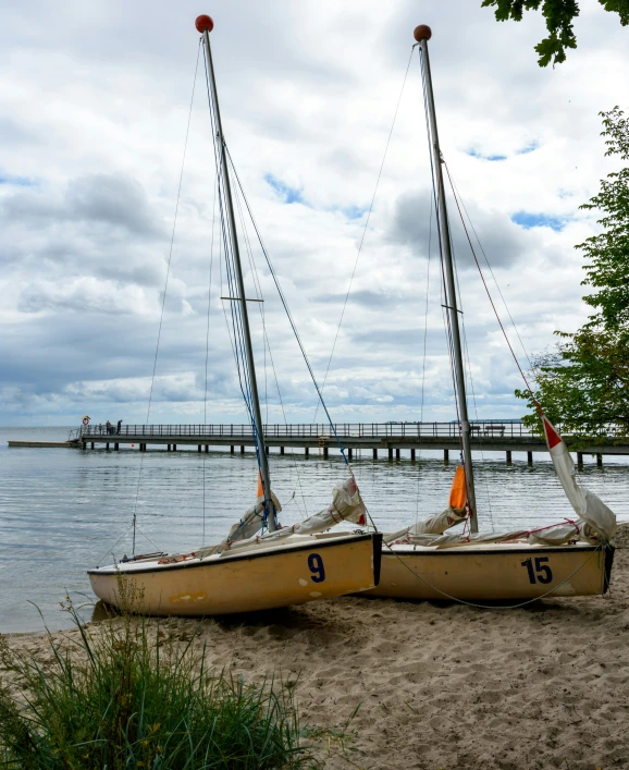 two sailboats are sitting on the beach near the water