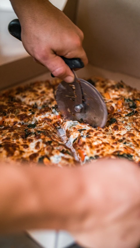 someone using a pastry cutter to slice a pizza