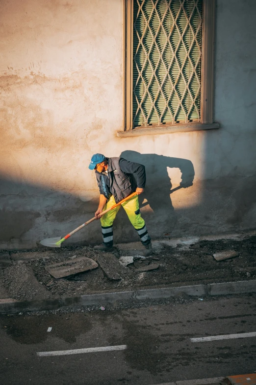 a man in safety gear walking down a street with a shovel