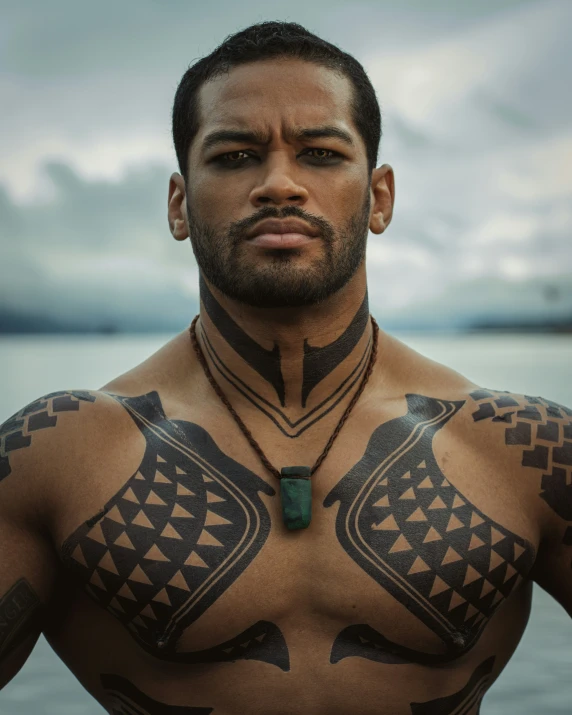 a man with tribal tattoos stands in front of the water