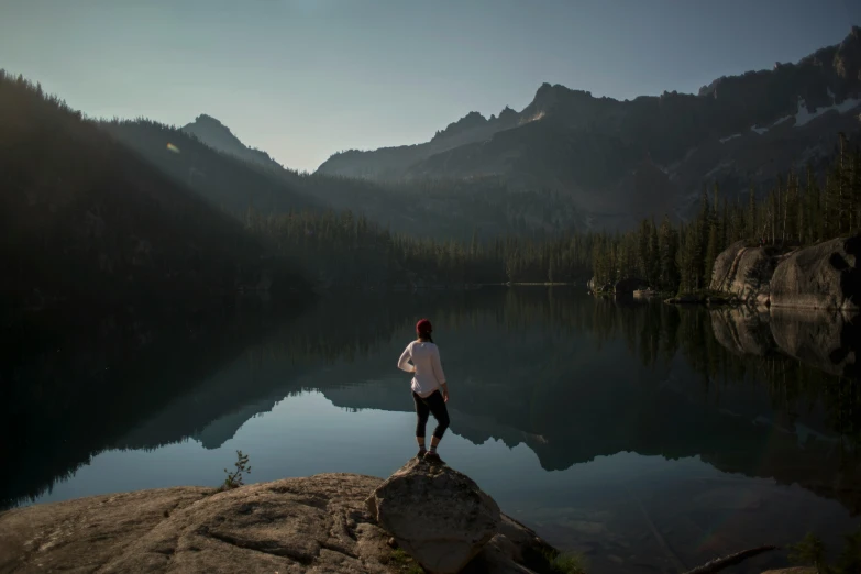 a man standing on top of a rock near a mountain lake