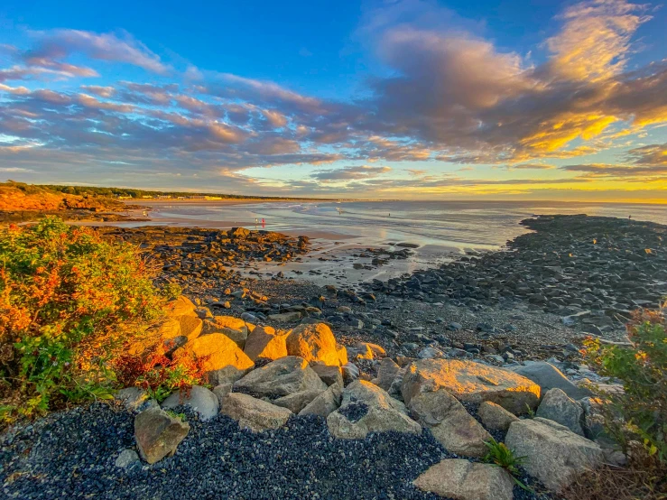 the view from a rocky beach near the ocean during a sunset