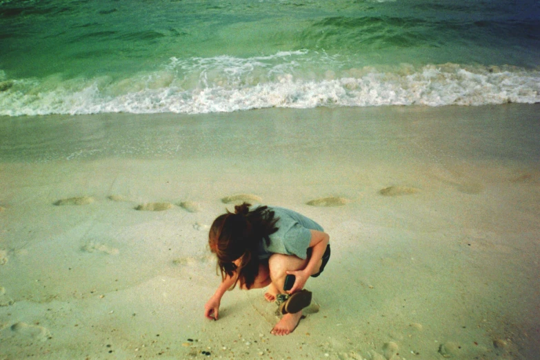 a young woman is bending over to paint her pictures on the sand