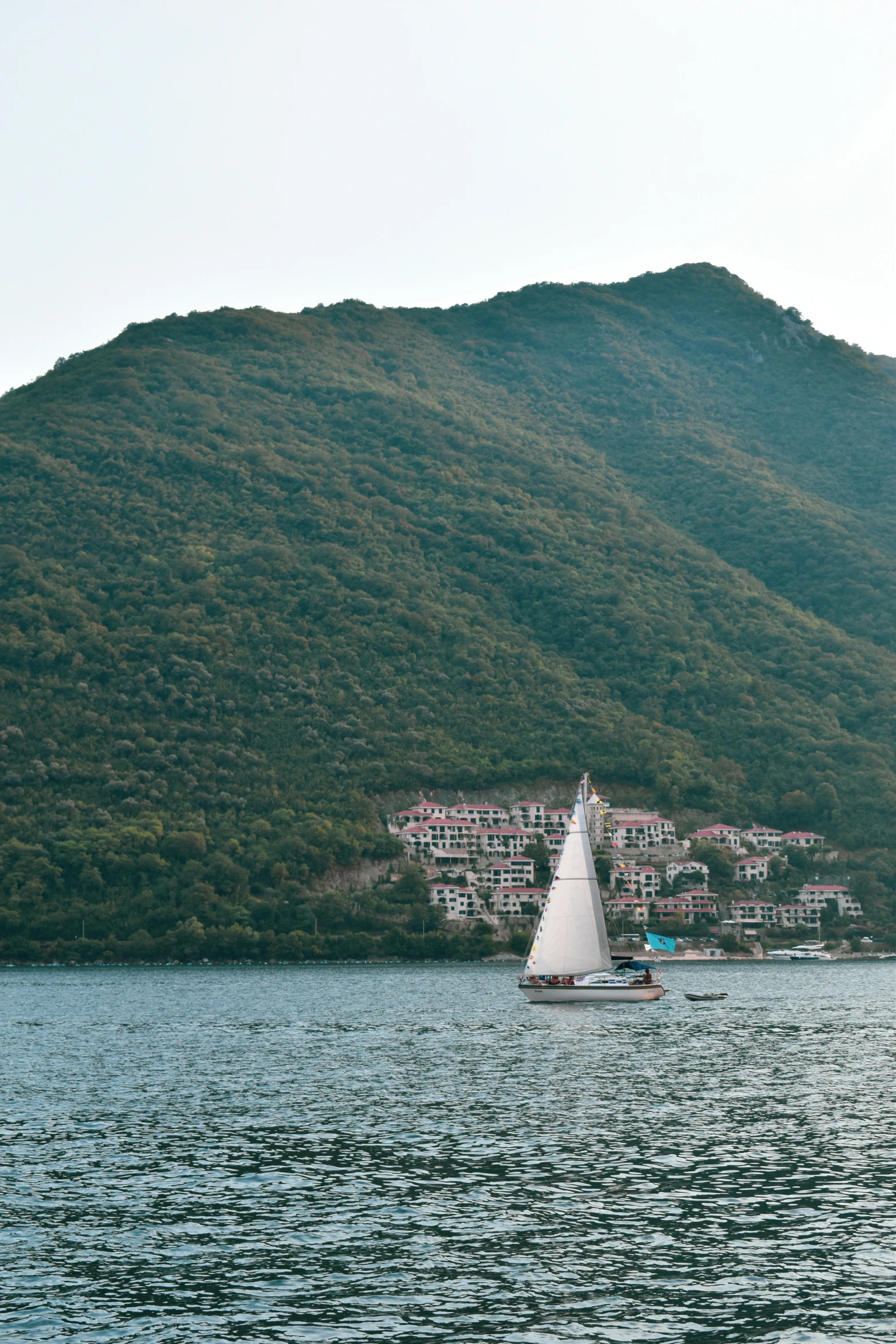 the sailboat is in the water by a mountainous coast