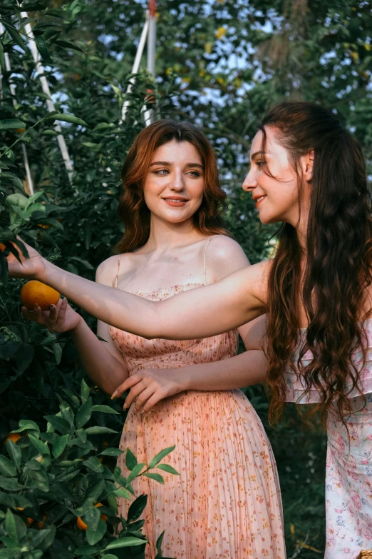 two pretty women touching each other by some oranges