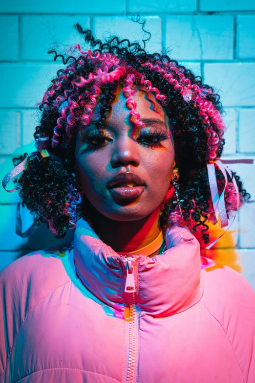 young woman with colorful hair and makeup stands in front of a brick wall