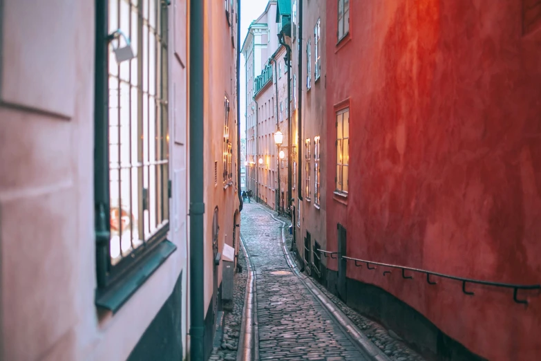 a narrow street with some red buildings and a clock tower in the background