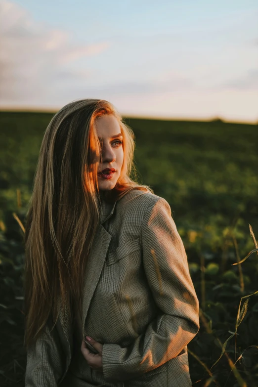 a girl standing in an open field with her hair blowing in the wind