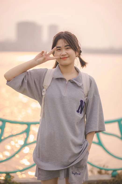 a woman making a peace sign while standing on the side of the river