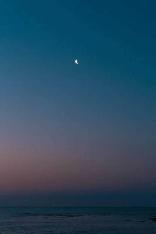 the moon shines bright in the evening sky over the ocean