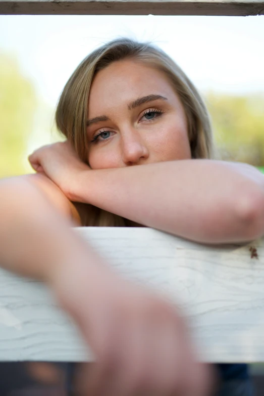 a woman with a long brown hair leans against a wooden structure