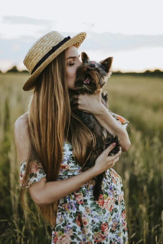 a girl wearing a hat kissing her puppy in a field