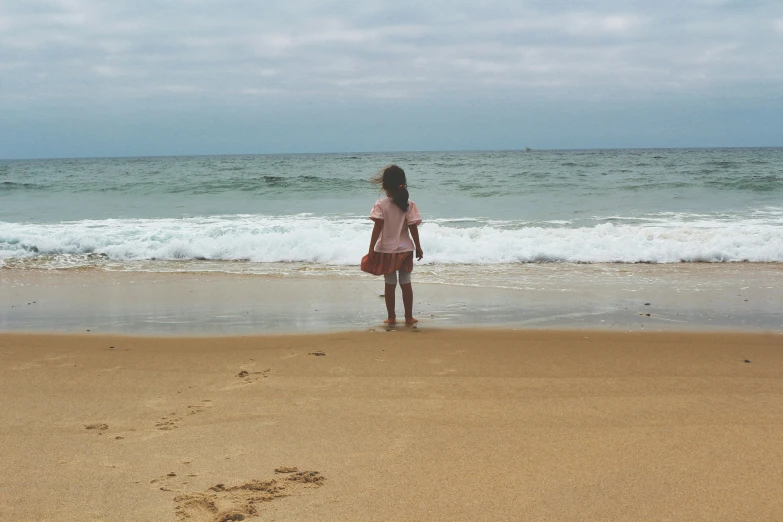 a little girl standing in the surf watching her footprints