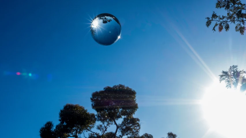 a chrome ball is floating in the air near trees