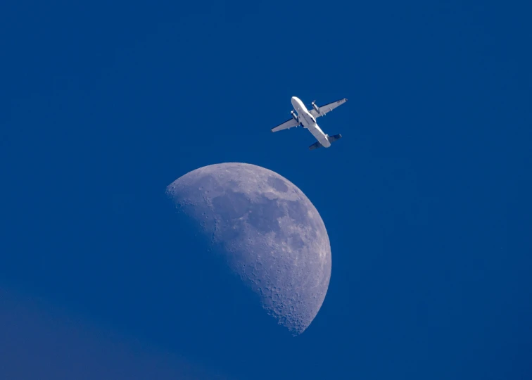 an airplane flying next to the moon against a blue sky