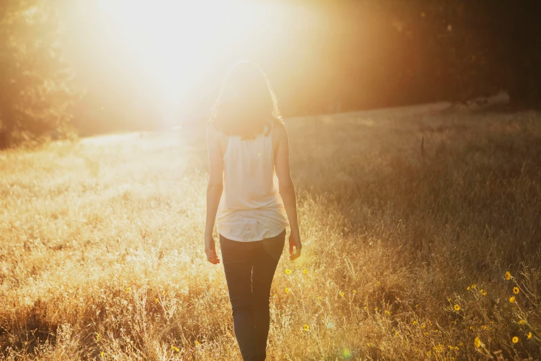 a woman walks through a field at sunset