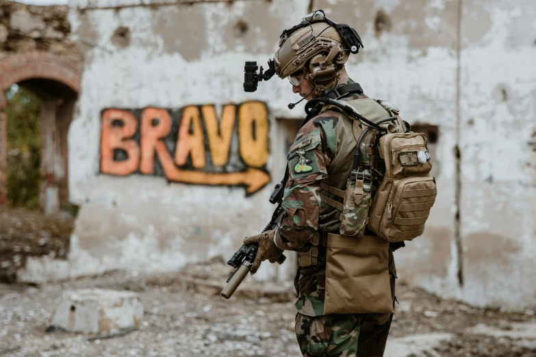 soldier in camouflage with rifle walking next to graffiti