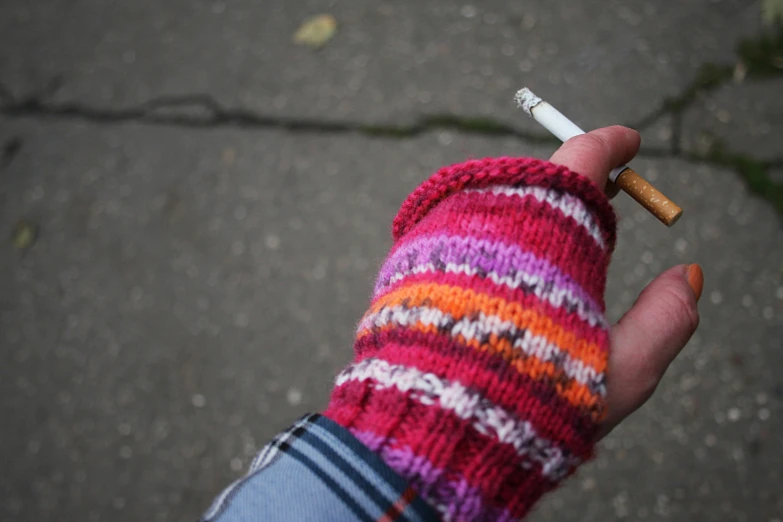 someone holding a cigarette with a multi colored knitted sleeve