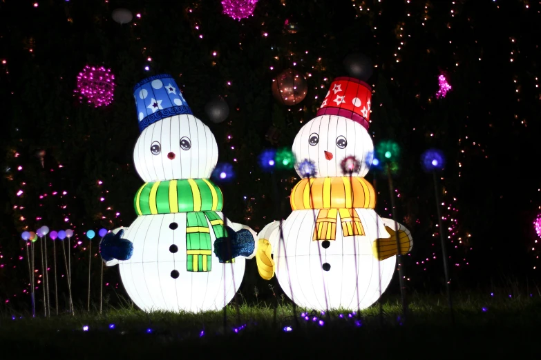 three snowmen with hats and scarfs standing by a fence