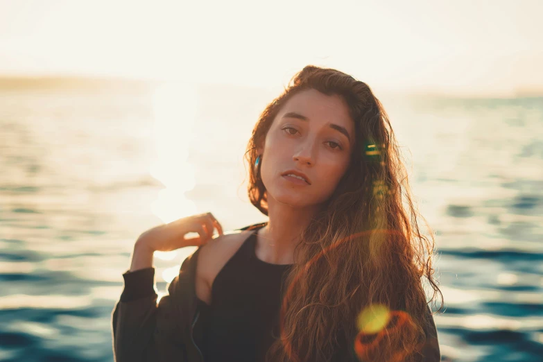 a girl standing on the shore with her hair blowing in the wind