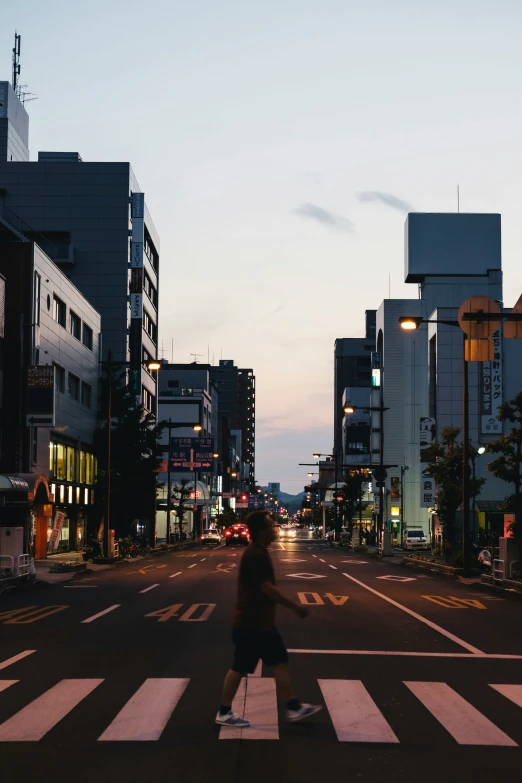 a woman crossing the street at sunset with a bag on her hip