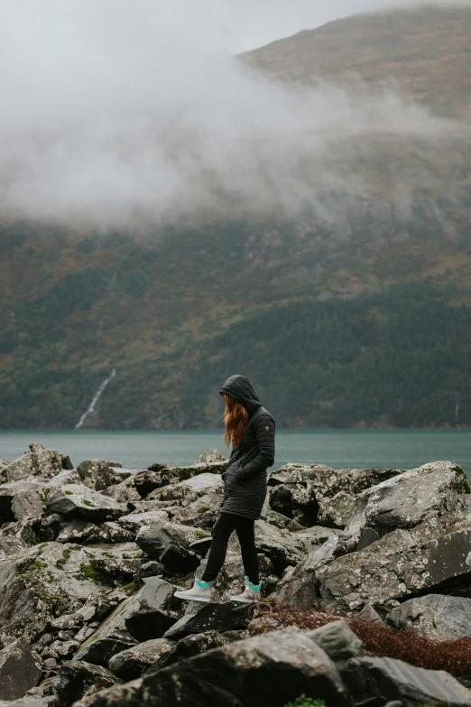 a girl stands on rocks by the water