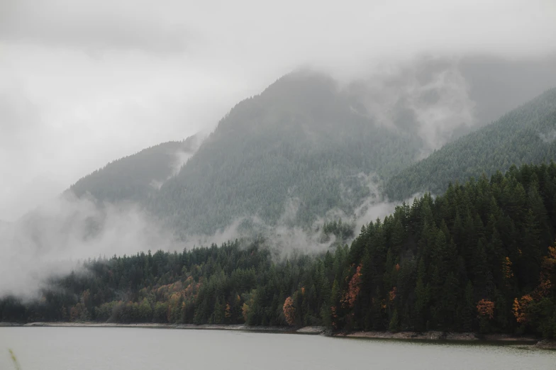 a lake surrounded by trees with clouds coming over