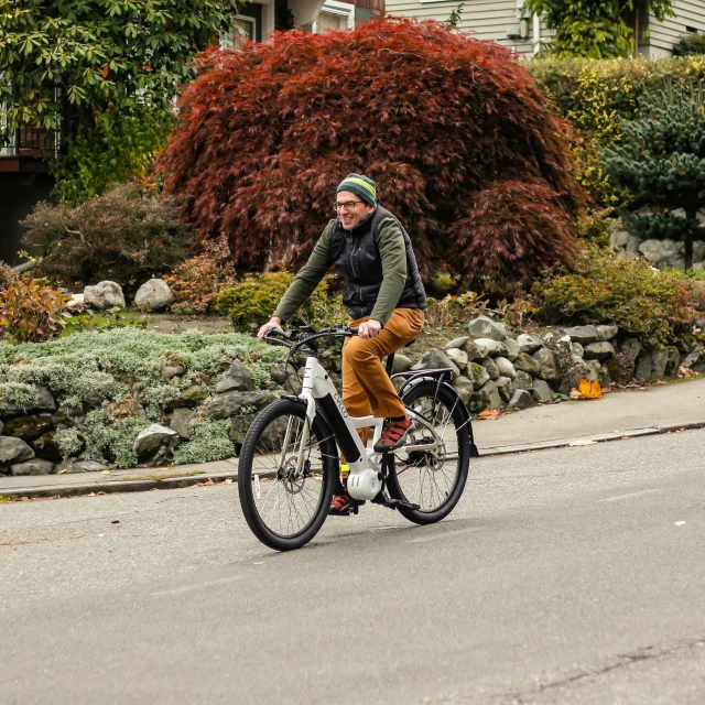 a man riding a bicycle on a street with trees and bushes behind him