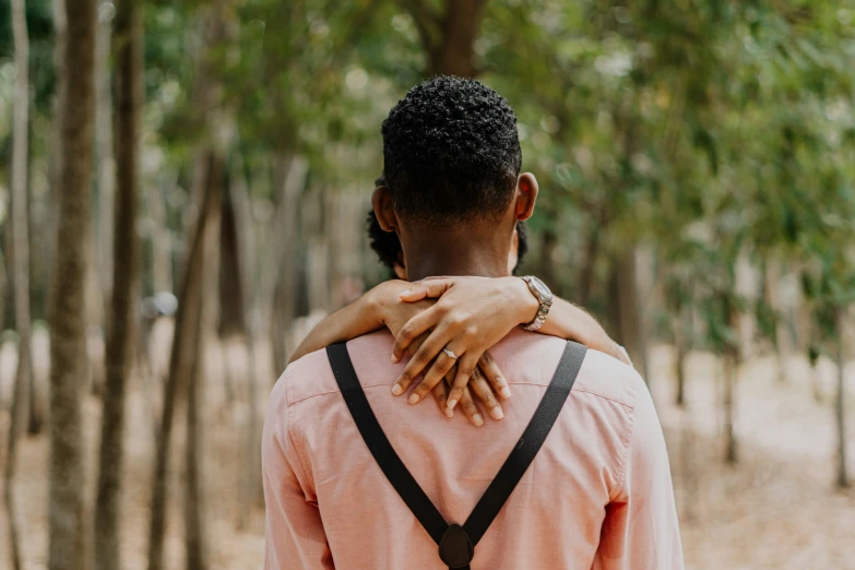 a person wearing a backpack is hugging another person in front of trees