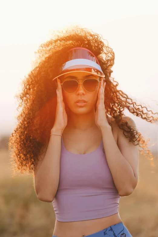 a young lady standing in a field wearing sunglasses and a hat