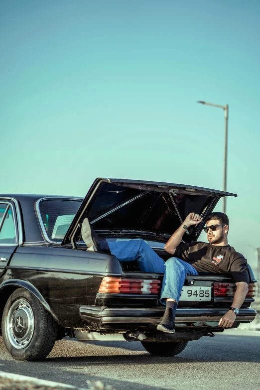 a man sits on the trunk of an old mercedes benz