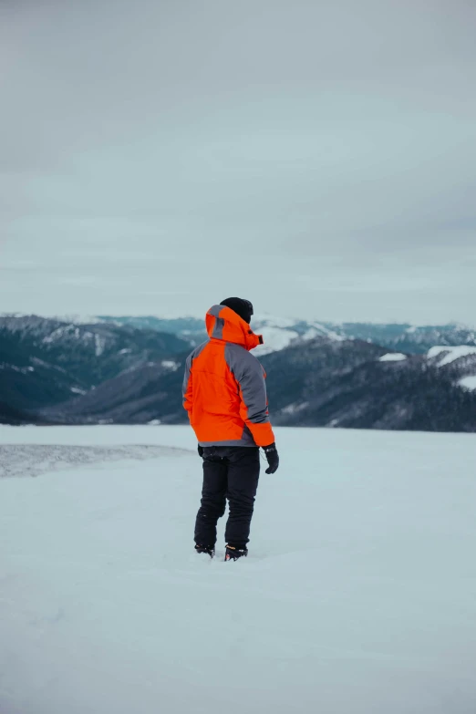 a man with orange jackets and black pants on top of a snow covered field