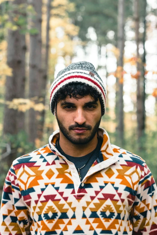 a man wearing a multicolored sweater in the woods