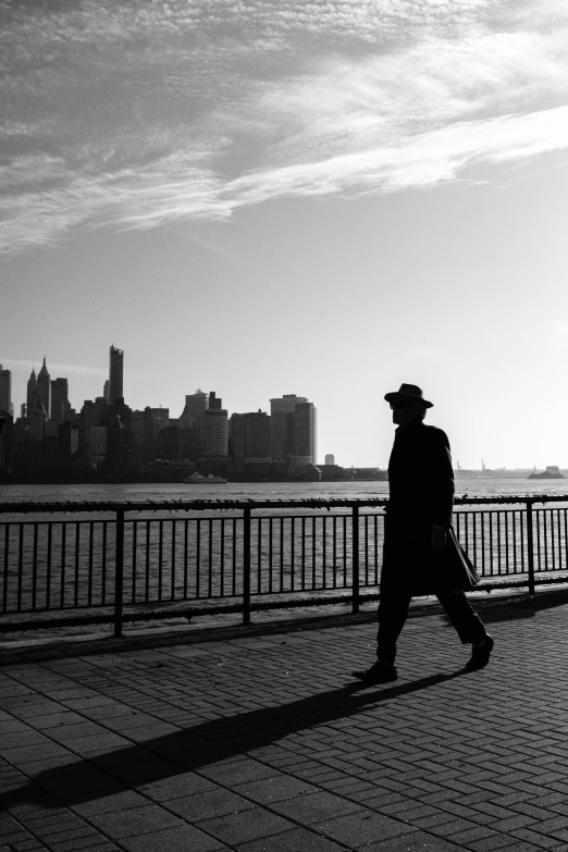 a man wearing a hat walks down a sidewalk next to a waterfront