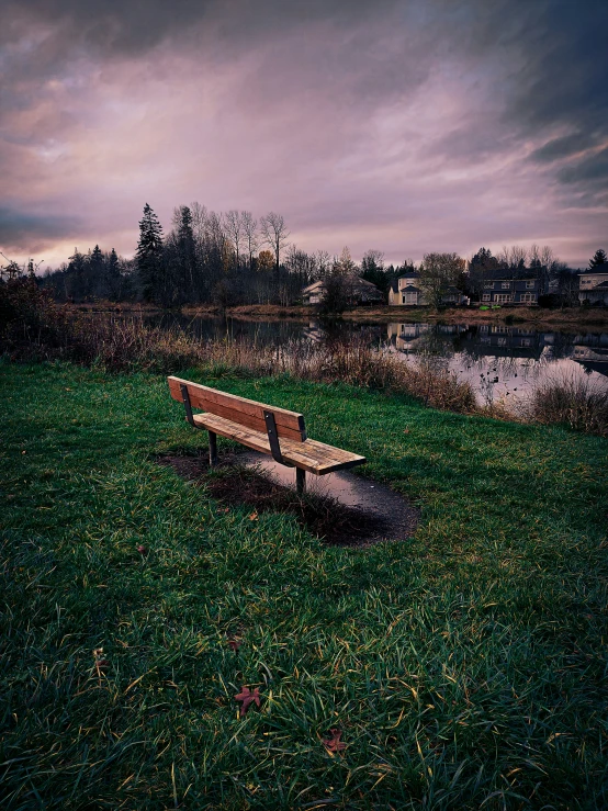 a park bench sits in the grass by a river