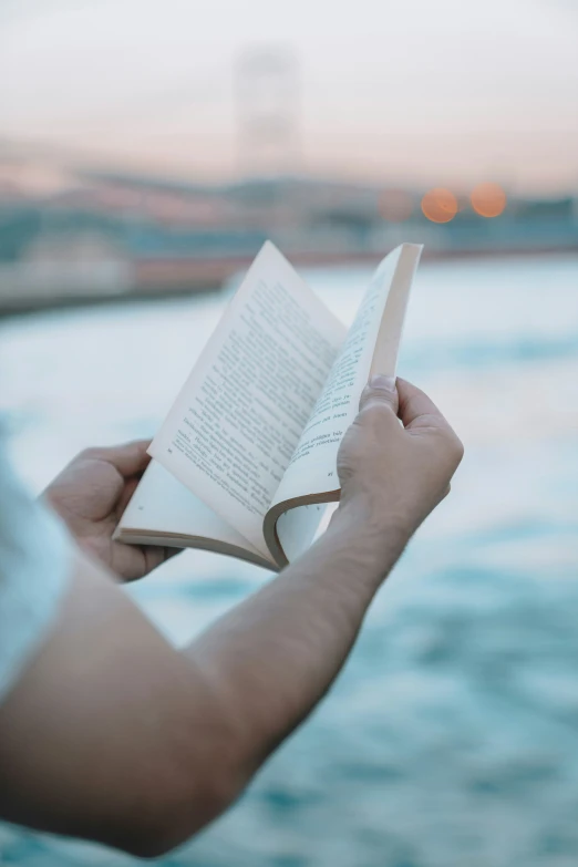 a person holding a book next to a body of water