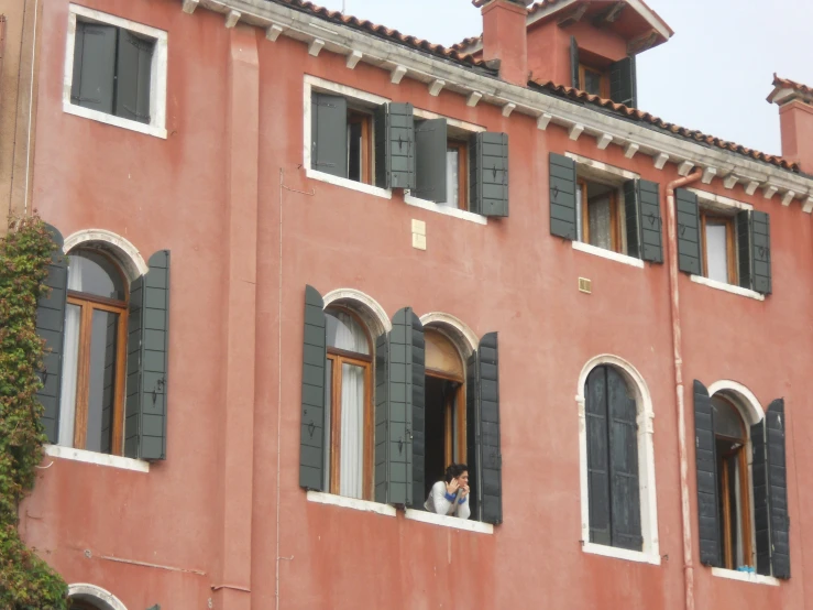 two people are standing at the window of a pink building