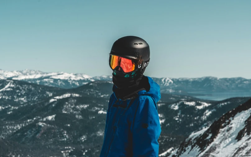 snowboarder wears goggles and stands on top of a mountain