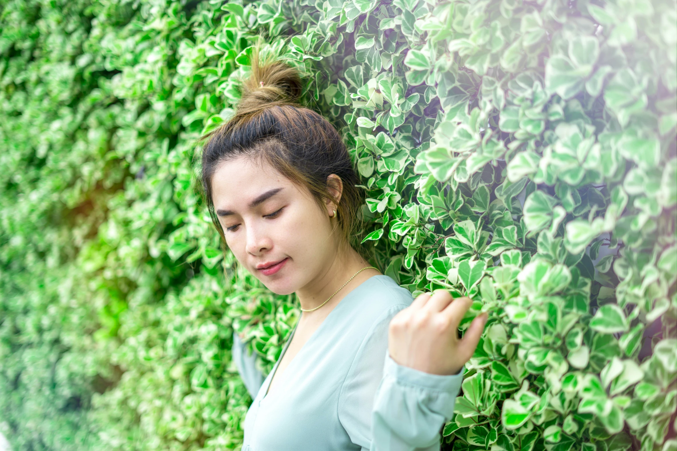 woman in green blouse standing by hedge, staring down