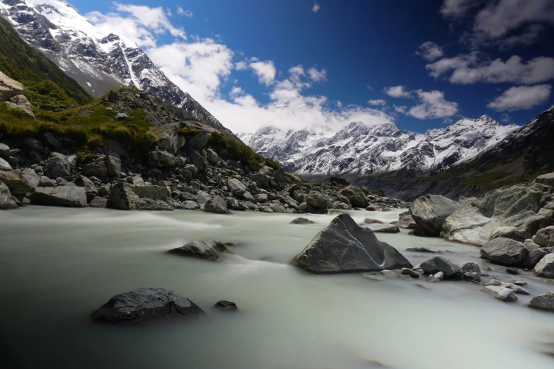 a body of water near some large rocks and snow covered mountains