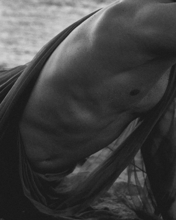 a black and white po of a shirtless man holding his head while laying on a beach