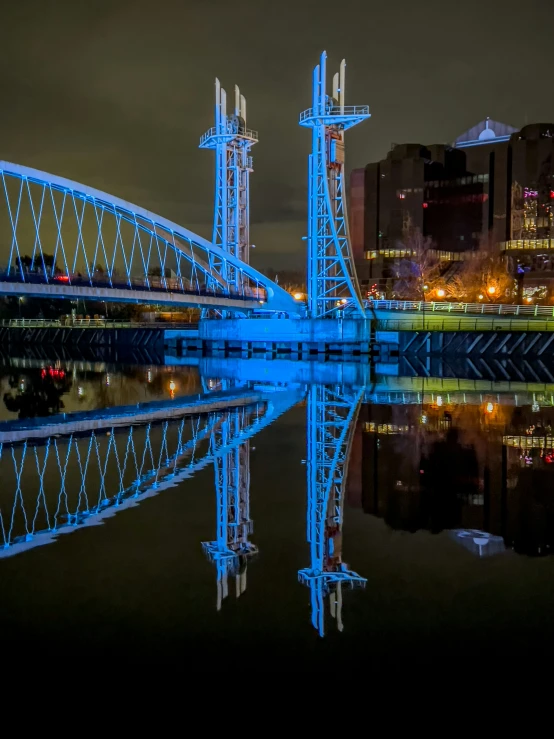 a long exposure s of a lit blue bridge reflecting on water