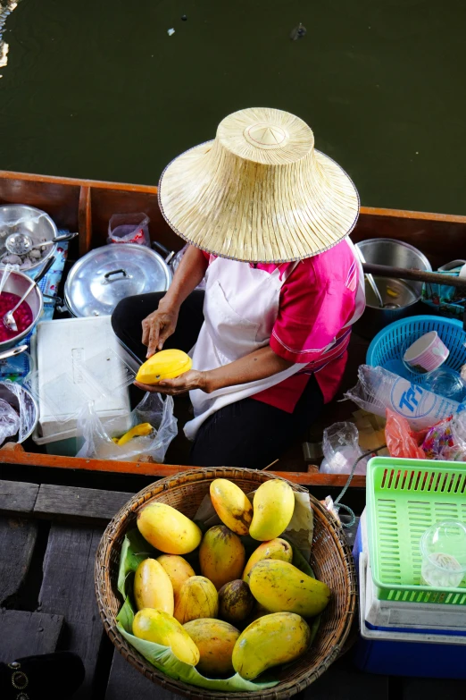 a lady wearing a straw hat is sitting by a basket of fruit