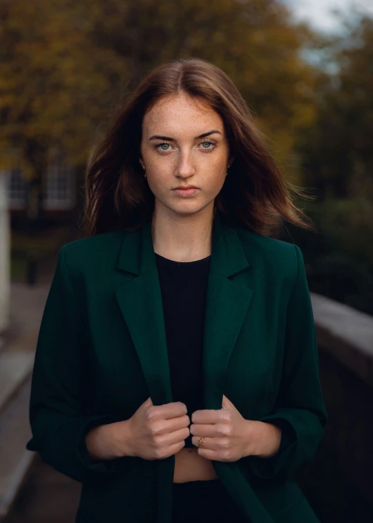 a woman in a dark suit and black shirt standing next to some trees