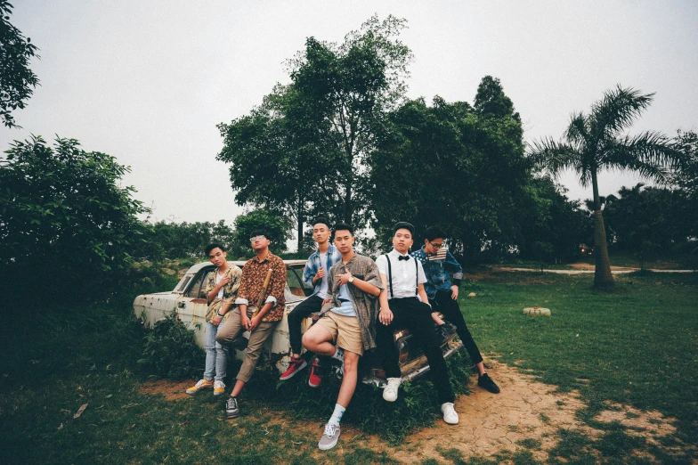 group of people sitting on a car on a grassy field