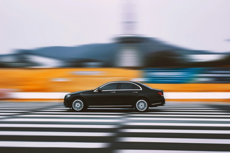 a black car on a road with buildings in the background